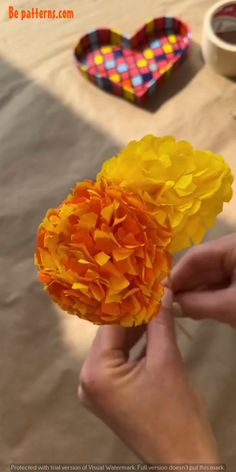 a person is holding a yellow flower in their hand with other items on the table behind them