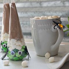 two candy cones with googly eyes are sitting next to a cup filled with marshmallows