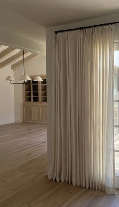 an empty room with white curtains and wooden floors