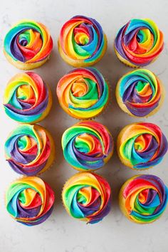 cupcakes with rainbow frosting are arranged on a white surface and placed in the shape of spirals