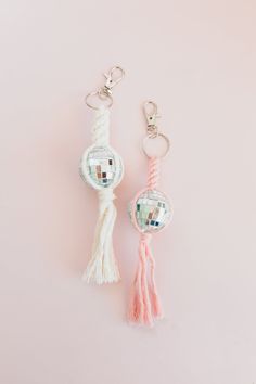 two keychains with tassels on them sitting next to each other in front of a pink background