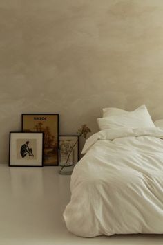 a bed with white sheets and pillows in a room next to pictures on the wall