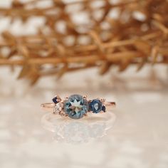 three stone ring sitting on top of a white surface next to a branch with branches in the background