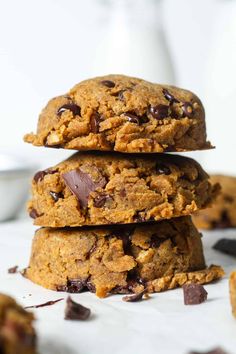 three cookies stacked on top of each other with chocolate chips scattered around them and milk in the background