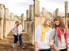 two young women standing next to each other in front of wooden poles and fence posts