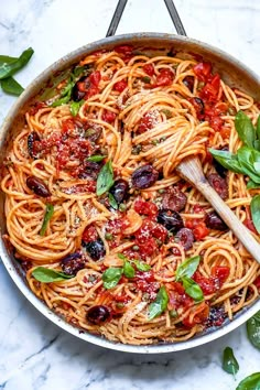 a skillet filled with pasta and olives on top of a marble countertop