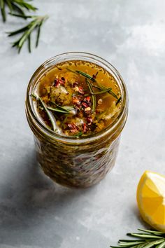 a glass jar filled with food next to a lemon wedge and rosemary sprig