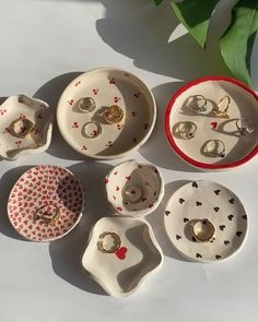 seven pieces of porcelain jewelry sitting on a white surface next to a green leafy plant