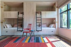 two bunk beds with ladders in a bedroom next to a red chair and rug