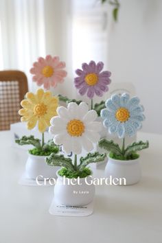 crocheted flowers in small white vases sitting on a table