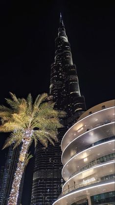 the burj building is lit up at night with palm trees in front of it