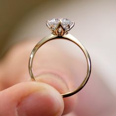 a close up of a person's hand holding a ring with a diamond on it