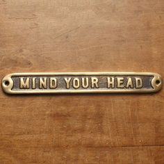 a metal sign that says mind your head on a wooden surface with rusted edges