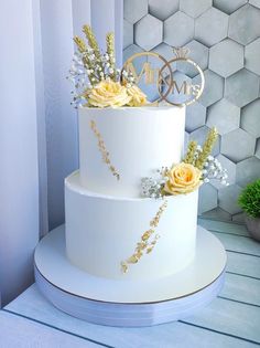 a three tiered white wedding cake with yellow flowers on the top and gold lettering