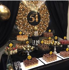 a table topped with lots of cakes and cupcakes next to a black curtain