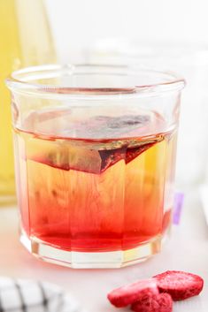 a glass cup filled with liquid next to two raspberries on a white table