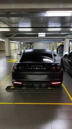 two cars parked in a parking garage with yellow lines painted on the floor and one is black