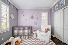 a baby's room decorated in lavender and gray with white trim, crib, rocking chair, teddy bear on chevron