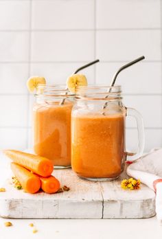 two mason jars filled with carrots and banana slices on top of a cutting board