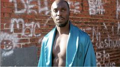 a man with no shirt on standing in front of a brick wall covered in graffiti