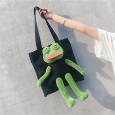 a person holding a black bag with a green stuffed frog on it's side