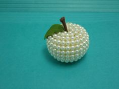 a white beaded apple sitting on top of a blue table next to a green leaf