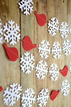 paper snowflakes are hung on a wooden wall with red hearts and birds hanging from them