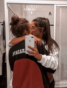 two women hug each other while taking a selfie in front of a bathroom mirror