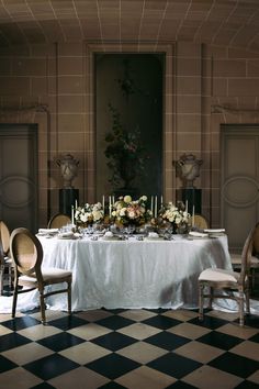 a dining room table set with flowers and candles on top of it, in front of two urns