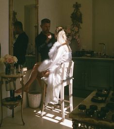 a woman sitting on a chair in front of a mirror next to a man standing behind her