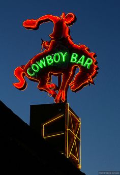 the neon cowboy bar sign is lit up in the night sky above it's roof