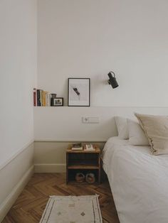 a bedroom with white walls and wooden flooring has a rug on the floor next to the bed