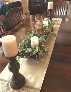 a dining room table with candles and greenery on the long centerpiece, along with an animal figurine