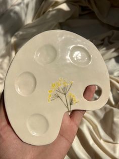 a hand holding a white ceramic plate with yellow flowers on the bottom and holes in the middle