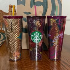 three starbucks cups sitting on top of a wooden table