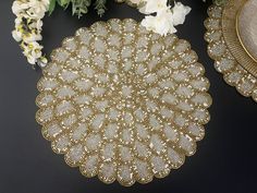 a gold doily next to some flowers on a black surface with white and yellow flowers in the background