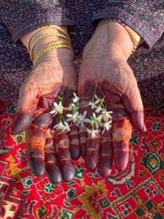 an old woman's hands with flowers in their palms on a colorful area rug