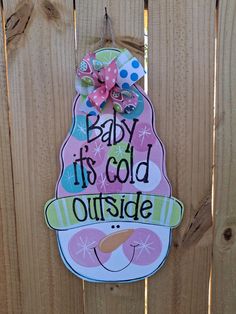 a baby its cold outside sign hanging on a wooden fence with a pink bow and polka dots