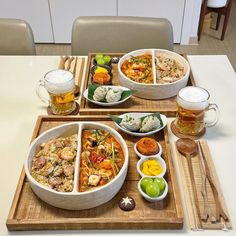 a table topped with bowls and plates filled with food next to glasses of beer on top of a wooden tray