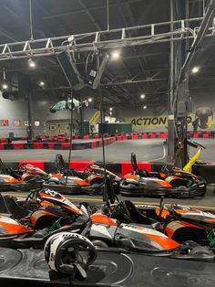 several orange and black go karts lined up in an indoor race track with lights on