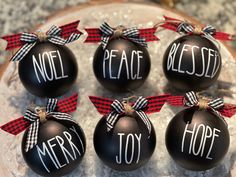 six black ornaments with red and white ribbon saying noel, peace, and joy on them