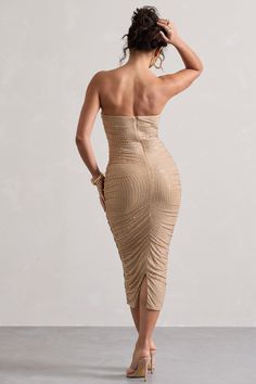 the back of a woman in a beige dress, with her hand on her head