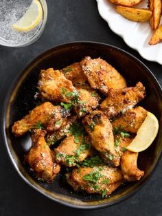 chicken wings in a pan with lemon wedges and parsley