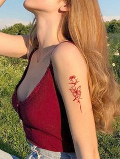 a woman sitting in the grass with a flower tattoo on her left arm and shoulder