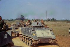 some soldiers are sitting on top of an army tank in the middle of a dirt field