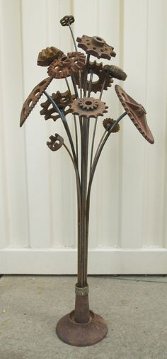 a metal sculpture with leaves on it in front of a white wall and flooring