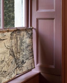 a curtain hanging on the side of a window sill in front of a pink door