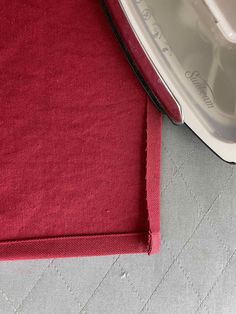 an iron is sitting on the floor next to a piece of red fabric that has been sewn