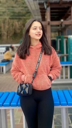 a woman standing next to a blue bench holding a black purse and looking at the camera