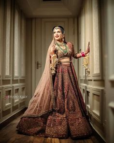 a woman in a red and gold bridal outfit posing for the camera with her hands on her hips